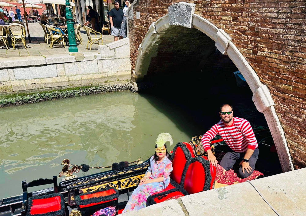 Gondolier mặc áo kẻ sọc điều khiển thuyền qua những con kênh nhỏ của Venice